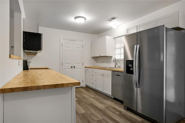 kitchen featuring wood-type flooring, butcher block counters, appliances with stainless steel finishes, sink, and white cabinets