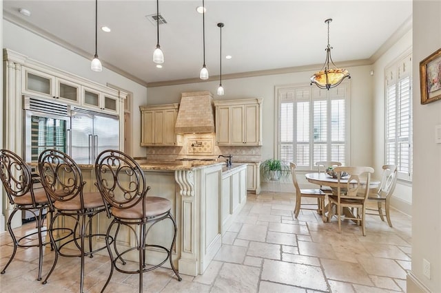 kitchen with tasteful backsplash, light stone counters, built in fridge, premium range hood, and a kitchen island