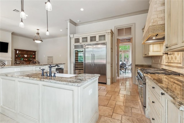 kitchen with light stone countertops, premium appliances, decorative light fixtures, a center island with sink, and custom range hood