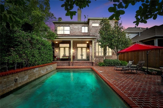 pool at dusk featuring a patio area and french doors