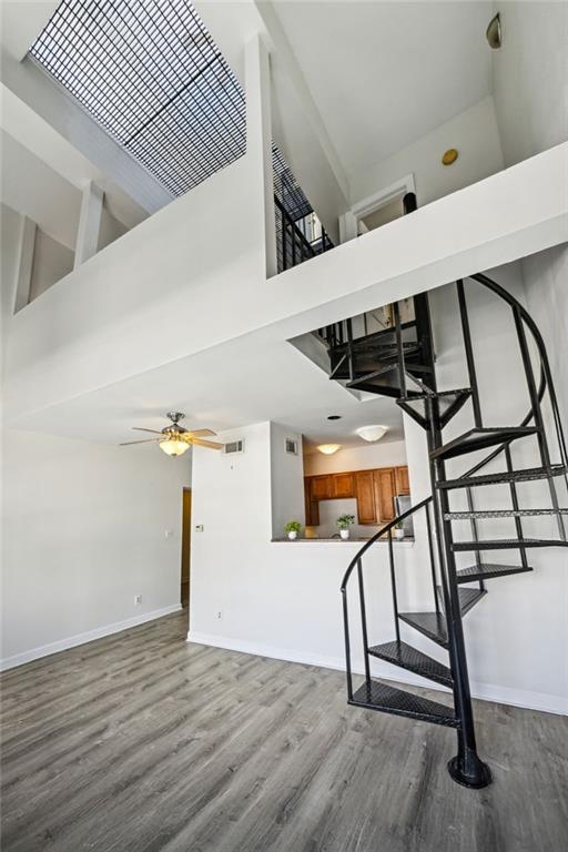 staircase with ceiling fan, a high ceiling, and wood-type flooring