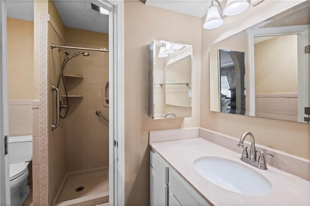 bathroom featuring a tile shower, vanity, a textured ceiling, and toilet