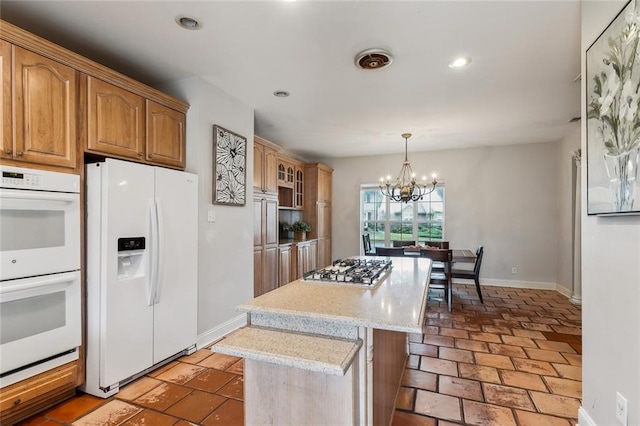 kitchen featuring light stone countertops, an inviting chandelier, hanging light fixtures, white appliances, and a center island