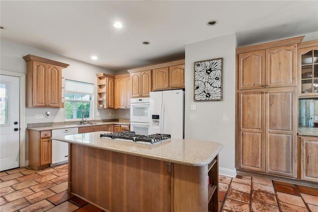 kitchen featuring light stone counters, a center island, white appliances, and sink