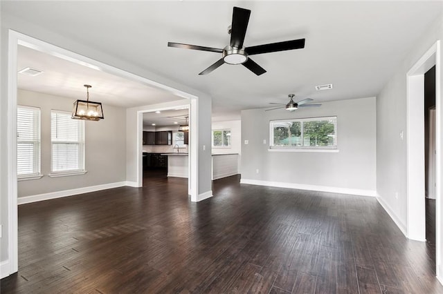 unfurnished living room featuring ceiling fan with notable chandelier and dark hardwood / wood-style flooring