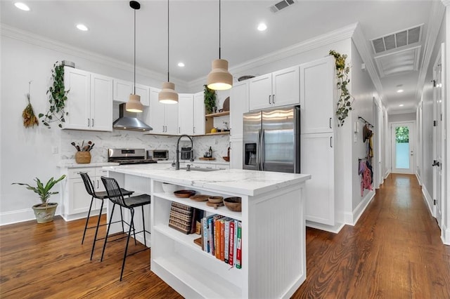 kitchen with white cabinetry, appliances with stainless steel finishes, wall chimney exhaust hood, and an island with sink