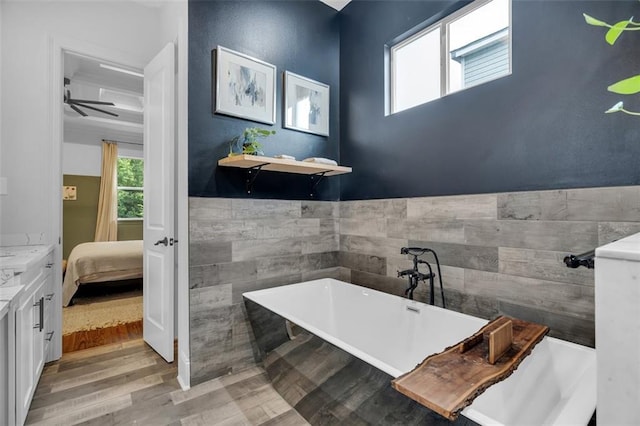 bathroom with tile walls, hardwood / wood-style flooring, vanity, ceiling fan, and a tub to relax in