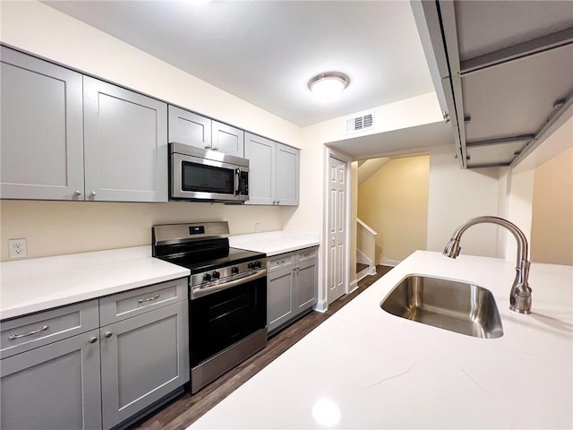 kitchen with dark wood-type flooring, light stone counters, sink, gray cabinets, and appliances with stainless steel finishes