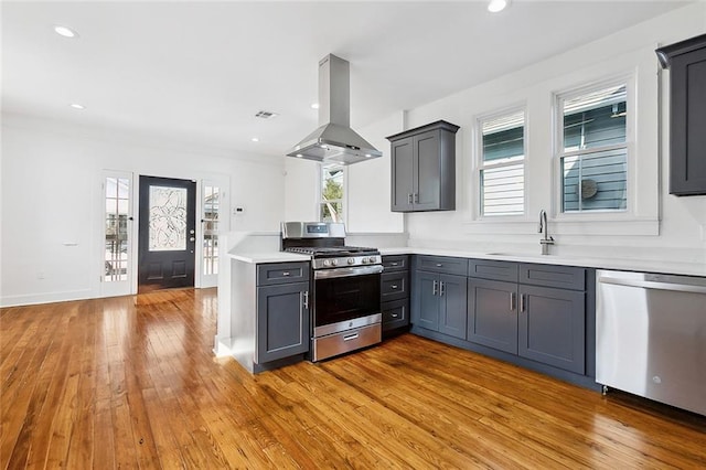 kitchen with island range hood, sink, gray cabinetry, light wood-type flooring, and appliances with stainless steel finishes