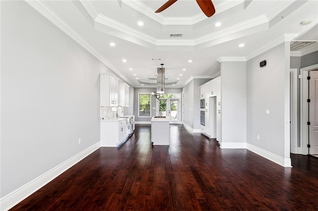 unfurnished living room featuring sink, ceiling fan with notable chandelier, a raised ceiling, crown molding, and dark wood-type flooring