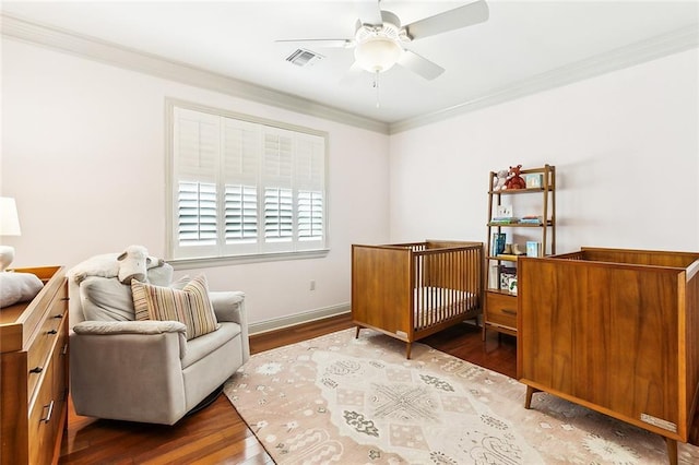 bedroom with ornamental molding, a nursery area, hardwood / wood-style flooring, and ceiling fan