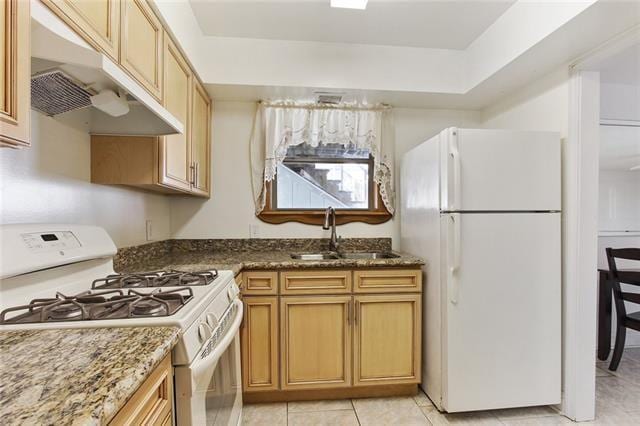 kitchen featuring light tile patterned flooring, white appliances, sink, dark stone countertops, and a tray ceiling