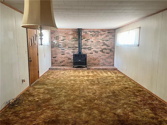 unfurnished living room with crown molding, wooden walls, a wood stove, and carpet floors