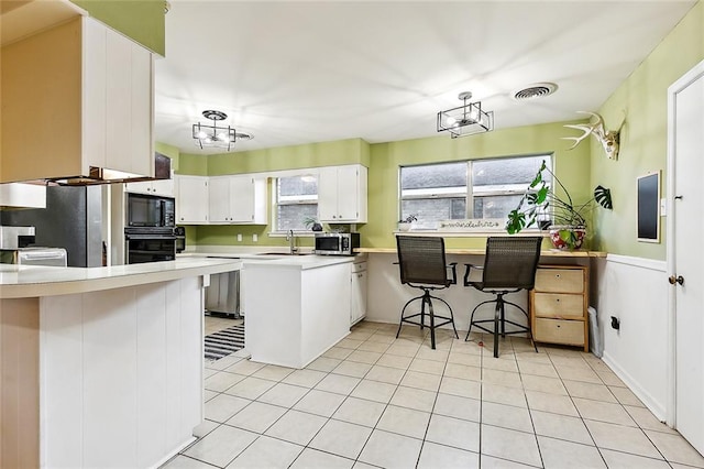 kitchen featuring white cabinets, kitchen peninsula, black appliances, a breakfast bar area, and sink