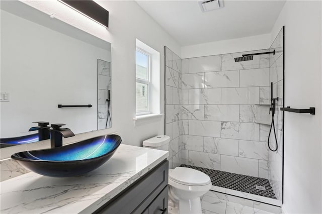 bathroom with toilet, a tile shower, and vanity