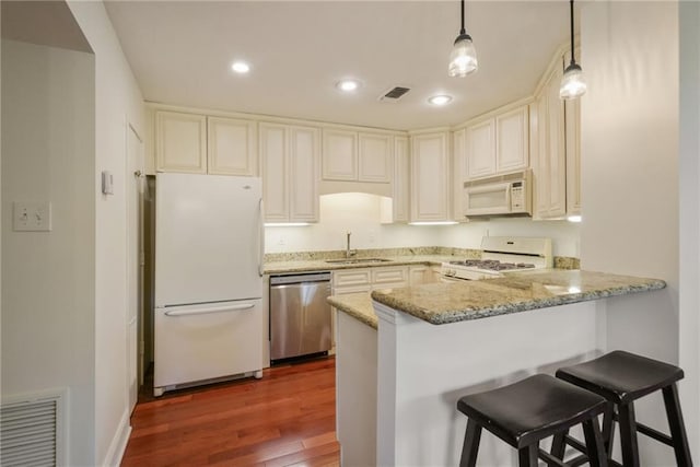 kitchen featuring sink, light stone countertops, dark hardwood / wood-style floors, decorative light fixtures, and white appliances