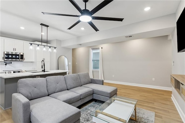 living room with ceiling fan, sink, and light hardwood / wood-style floors