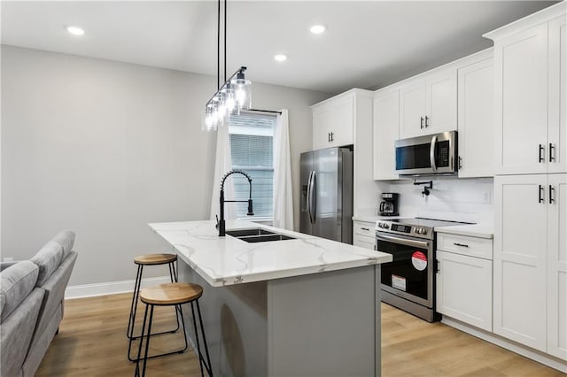 kitchen featuring a center island with sink, stainless steel appliances, white cabinetry, decorative light fixtures, and sink