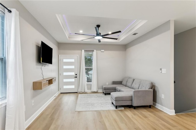 living room featuring a raised ceiling, ceiling fan, and light hardwood / wood-style flooring