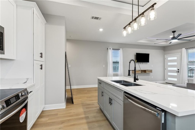 kitchen featuring light hardwood / wood-style floors, light stone counters, sink, an island with sink, and appliances with stainless steel finishes