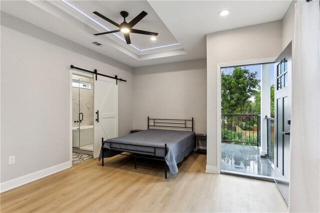 bedroom featuring ensuite bath, a barn door, ceiling fan, and light hardwood / wood-style flooring