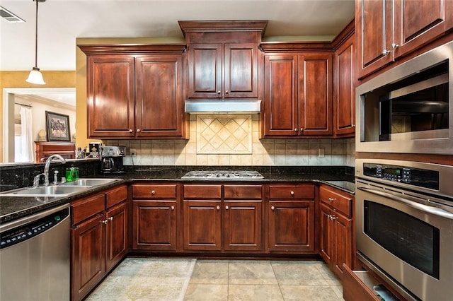 kitchen with pendant lighting, backsplash, appliances with stainless steel finishes, a sink, and under cabinet range hood