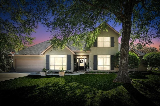 traditional home with driveway, a garage, a shingled roof, a lawn, and stucco siding