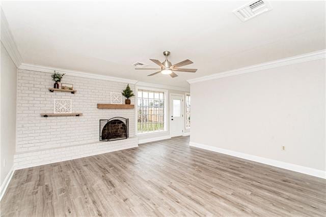 unfurnished living room with ceiling fan, wood-type flooring, a brick fireplace, and crown molding