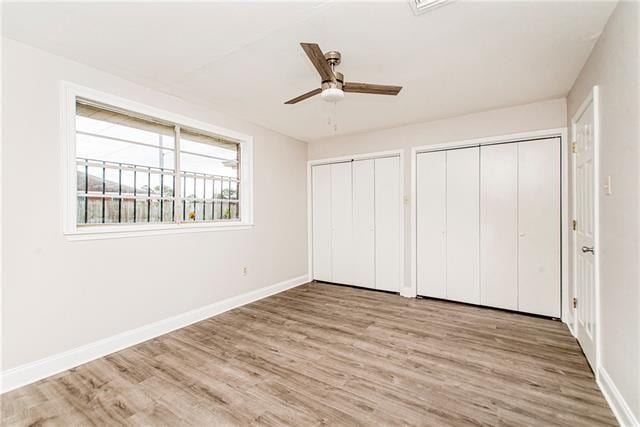 unfurnished bedroom featuring light hardwood / wood-style floors, ceiling fan, and two closets