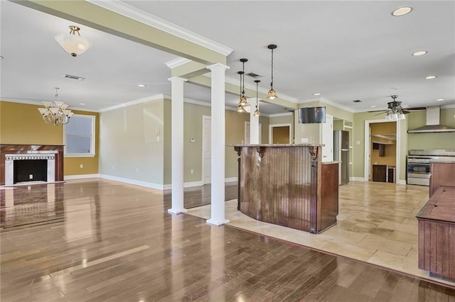 kitchen featuring decorative columns, a fireplace, freestanding refrigerator, stainless steel range oven, and wall chimney range hood