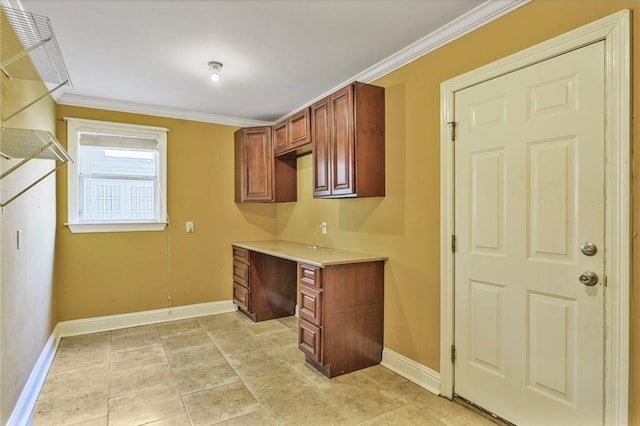 kitchen featuring baseboards, ornamental molding, light countertops, and built in desk