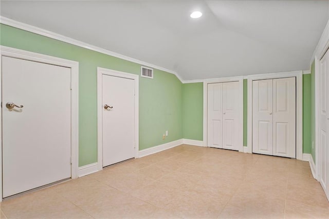 unfurnished bedroom with baseboards, visible vents, vaulted ceiling, crown molding, and two closets