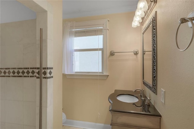 bathroom with baseboards, tiled shower, vanity, and toilet