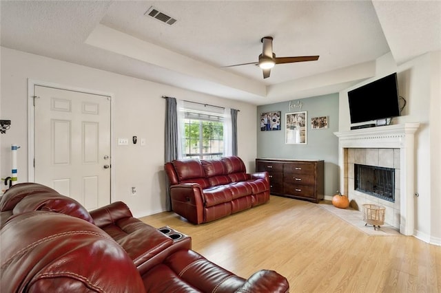 living room with a fireplace, ceiling fan, a raised ceiling, and light wood-type flooring