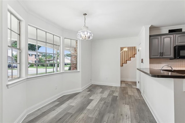 unfurnished dining area with an inviting chandelier, sink, crown molding, and light hardwood / wood-style flooring