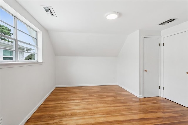 additional living space featuring lofted ceiling, light wood-type flooring, and a healthy amount of sunlight