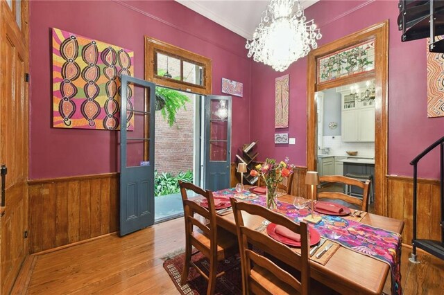 820B Saint Ann St, New Orleans, LA 70116 - dining space with a wainscoted wall, a chandelier, light wood-type flooring, wood walls, and ornamental molding