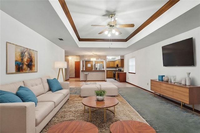 living room featuring ceiling fan, a raised ceiling, light wood-type flooring, and ornamental molding