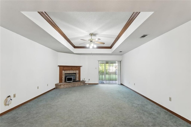 unfurnished living room with a raised ceiling, a brick fireplace, ceiling fan, ornamental molding, and carpet floors