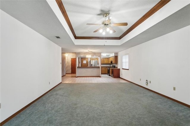 unfurnished living room featuring ceiling fan, ornamental molding, light carpet, and a tray ceiling