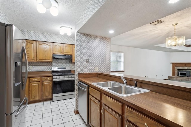 kitchen with a notable chandelier, sink, a textured ceiling, appliances with stainless steel finishes, and decorative light fixtures