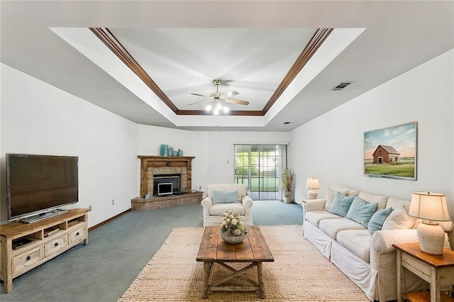 carpeted living room featuring a brick fireplace, a raised ceiling, ceiling fan, and ornamental molding