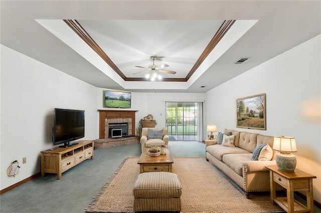 carpeted living room featuring a tray ceiling, ceiling fan, a fireplace, and ornamental molding