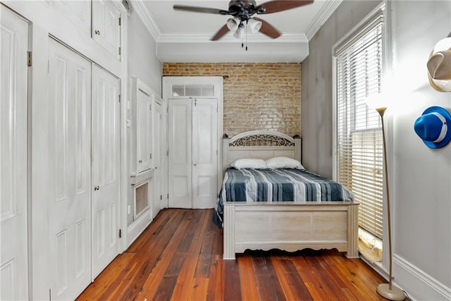 bedroom featuring dark wood-type flooring, two closets, ornamental molding, ceiling fan, and brick wall