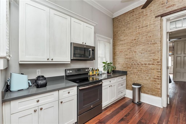 kitchen with crown molding, appliances with stainless steel finishes, dark hardwood / wood-style flooring, white cabinets, and brick wall