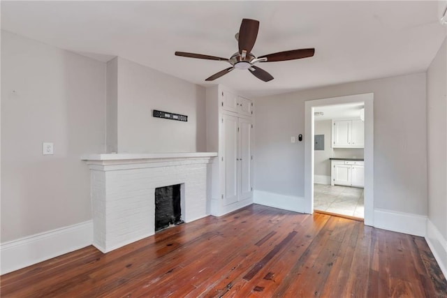 unfurnished living room featuring a brick fireplace, wood-type flooring, and ceiling fan