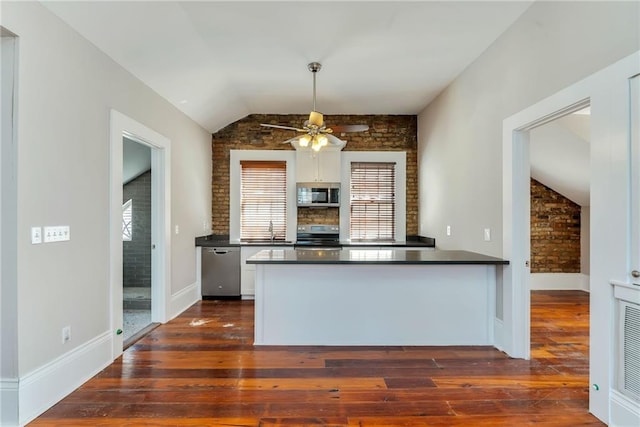 kitchen with dark wood-type flooring, appliances with stainless steel finishes, vaulted ceiling, and brick wall