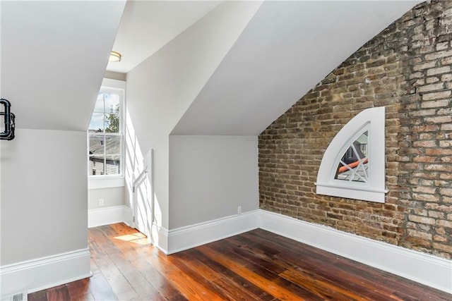 bonus room with dark wood-type flooring, brick wall, and lofted ceiling