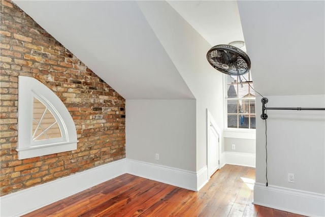 additional living space with vaulted ceiling, light hardwood / wood-style floors, and brick wall