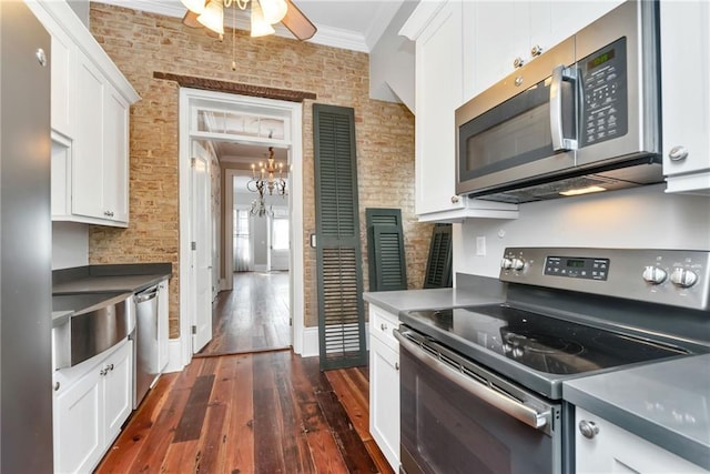 kitchen with white cabinets, appliances with stainless steel finishes, dark hardwood / wood-style floors, and brick wall